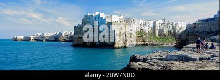 POLIGNANO A MARE, ITALIA - 29 MARZO 2018: Persone in riva al mare Adriatico con spettacolare vista di scogliere con grotte che si innalzano dal mare Adriatico a Pol Foto Stock