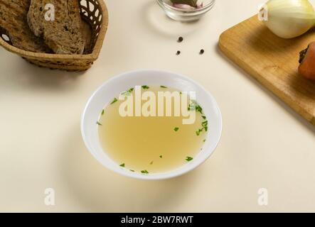 Bouillon fresco in un piatto bianco con erbe e crostini di pane di grano. Zuppa calda a base di carne, carote, cipolle, aglio e pepe. Orientamento orizzontale Foto Stock