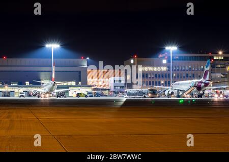 Vorfeld des Flughafen Stuttgart bei Nacht mit Schriftzug 'tuttgart' im Hintergrund - D-ABZE Eurowings Airbus A320-216 & OE-LWA Austrian Airlines Embr Foto Stock