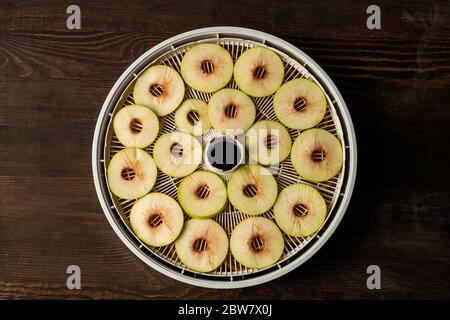 Disposizione piatta del vassoio circolare di plastica dell'asciugatore di frutta con le fette delle mele fresche sopra il tavolo di legno marrone che può essere usato come sfondo Foto Stock