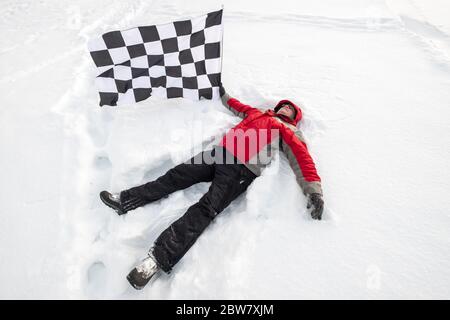 L'uomo giace nella neve con la bandiera del traguardo Foto Stock