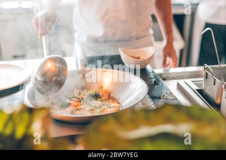 Primo piano di lavoro chef che prepara cibo cinese, cibo frittura in wok pain. Interni del ristorante asiatico. Foto Stock