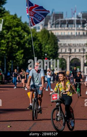 Londra, Regno Unito. 30 maggio 2020. Un uomo con una bandiera di jack di ringraziamento NHS Union segue un gruppo di biciclette a noleggio santander - godendosi in bicicletta sul Mall come il sole esce di nuovo. Il "blocco" continua per l'epidemia di Coronavirus (Covid 19) a Londra. Credit: Guy Bell/Alamy Live News Foto Stock