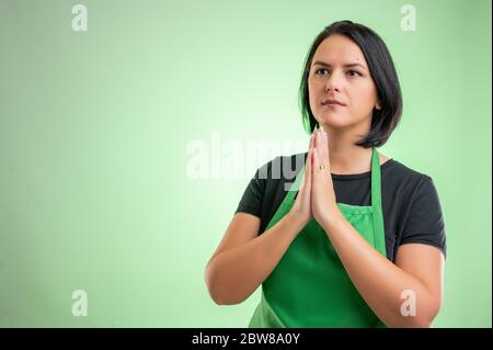 Cuoca femminile con grembiule verde e t-shirt nera, orante isolato su sfondo verde Foto Stock