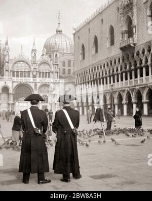 ANNI '30 DUE MEMBRI DELL'ARMA DEI CARABINIERI IN UNIFORME STORICA IN PIAZZA SAN MARCO VICINO AL PALAZZO DUCALE VENEZIA ITALIA - R5116 HAR001 HARS NELLE VICINANZE OCCUPAZIONI PALAZZO UNIFORMI MEMBRI ELEGANTI DEI POLIZIOTTI POLIZIOTTI COPPE INI MID-ADULT MID-ADULT UOMO PICCIONI BADGE BADGE NERO E BIANCO HAR001 MARCO VECCHIO STILE PIAZZA Foto Stock
