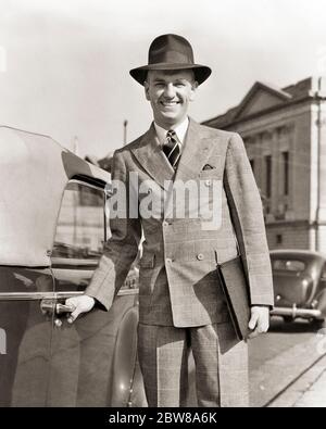 1940 SORRIDENTE VENDITORE IN VIAGGIO GUARDANDO LA FOTOCAMERA CHE INDOSSA DOPPIO VESTITO BREASTED MANO SULLA MANIGLIA PER APRIRE LA PORTA CONVERTIBILE DELL'AUTOMOBILE - S1381 HAR001 VEICOLO STILE HARS DOPPIO SODDISFATTO GIOIA LIFESTYLE SODDISFAZIONE CASA VITA COPIA SPAZIO MEZZA LUNGHEZZA PERSONE AUTOMOBILE MASCHI FIDUCIA TRASPORTO B&W OCCHIO CONTATTO SUCCESSO COLLETTO BIANCO VESTITO E VENDITA CRAVATTA FELICITÀ ALLEGRO AUTOS ORGOGLIO OCCUPAZIONI SORRISI VIAGGIARE AUTOMOBILI MANEGGIARE GIOIOSO ELEGANTE VEICOLI ALLEVATI A METÀ ADULTO MEDIO-ADULTO UOMO VENDITORI NERO E BIANCO CAUCASICO ETNIA HAR001 VECCHIO PORTAFOGLIO MODA Foto Stock