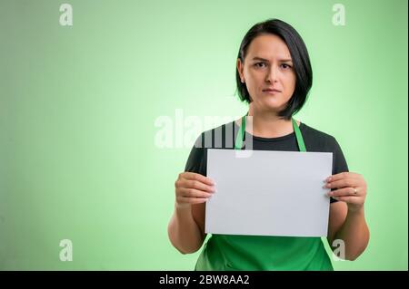 Cuoca con grembiule verde e t-shirt nera, tenendo un foglio bianco isolato su sfondo verde Foto Stock
