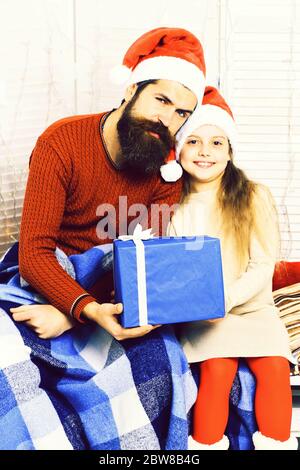 bell'uomo con barba lunga nel cappello rosso di natale con plaid a scacchi blu che tiene grande presente e bella ragazza bionda offesa in abito beige con mani incrociate, su sfondo bianco studio Foto Stock