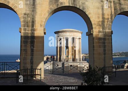 GIARDINI DI LOWER BARRAKKA, VALLETTA, MALTA - 16 NOVEMBRE 2019: Il monumento alla Guerra della Campana di Assedio visto attraverso un arco. Costruito nel 1992 per commemorare il Foto Stock