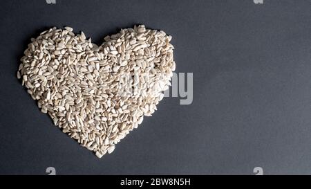 Vista dall'alto dei semi di girasole a forma di cuore su sfondo nero. Forma del cuore closeup dai semi. Foto Stock