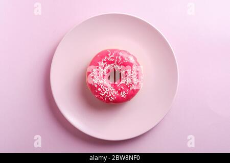 Ciambella rosa rossa con spruzzette bianche su piatto rosa, dessert con dolci piatti glassati su sfondo rosa minimo, vista dall'alto Foto Stock