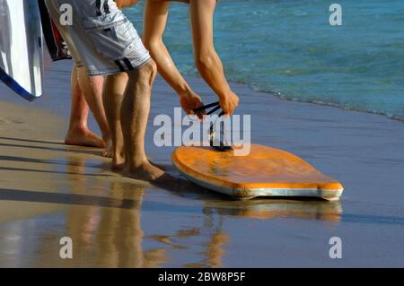 Boogie Boarder si prepara a cavalcare le onde. Lui e gli amici condividono l'uso del boogie arancione bordo. Foto Stock