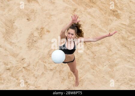 Giovane donna con palla bianca che gioca a pallavolo sulla spiaggia. Vacanza estiva e concetto sportivo Foto Stock
