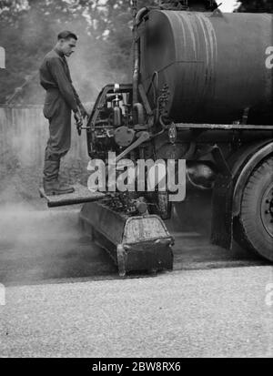 I lavoratori utilizzano una macchina per la spruzzatura di catrame di Taroads Limited per la superficie di una strada . 1938 Foto Stock