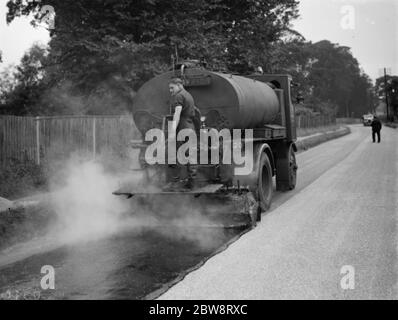 I lavoratori utilizzano una macchina per la spruzzatura di catrame di Taroads Limited per la superficie di una strada . 1938 Foto Stock