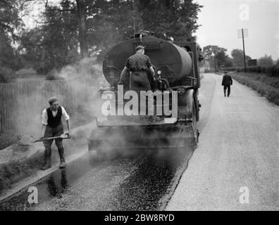 I lavoratori utilizzano una macchina per la spruzzatura di catrame di Taroads Limited per la superficie di una strada . 1938 Foto Stock