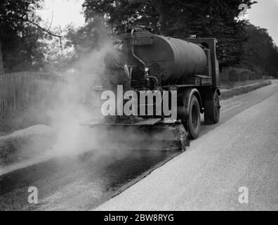 I lavoratori utilizzano una macchina per la spruzzatura di catrame di Taroads Limited per la superficie di una strada . 1938 Foto Stock