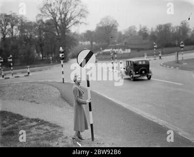 Una donna tiene un segnale di limite di velocità in corrispondenza di un incrocio stradale . 1938 Foto Stock