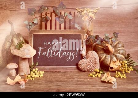 Decorazioni rustiche autunnali, testo 'Happy Fallidays' su una lavagna. Raccolta naturale del Ringraziamento. Foglie d'autunno, zucca, cuore decorativo in legno Foto Stock
