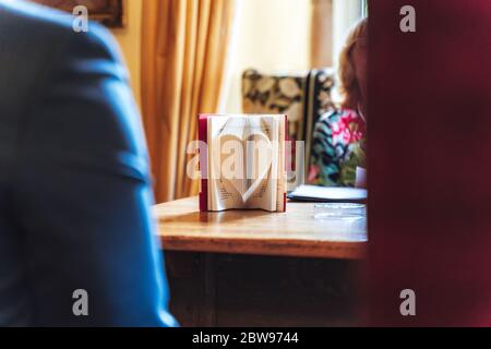 Apri il libro in piedi sul tavolo. Pagine del libro piegate a forma di cuore. Simbolo dell'amore. Foto Stock
