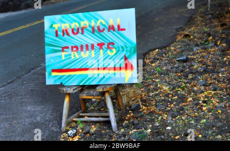 Il segno colorato siede sulla sedia rustica che fa pubblicità ai frutti tropicali sulla grande isola delle Hawaii. Il segno è acqua con fronte di palma. Le lettere sono gialle e rosse Foto Stock