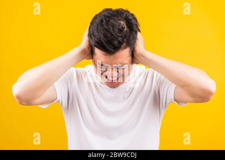 Ritratto giovane Aaian bello in piedi indossando la t-shirt bianca che copre le sue orecchie con le mani e urlando bocca aperta gamberetti espressione infastidita, Foto Stock