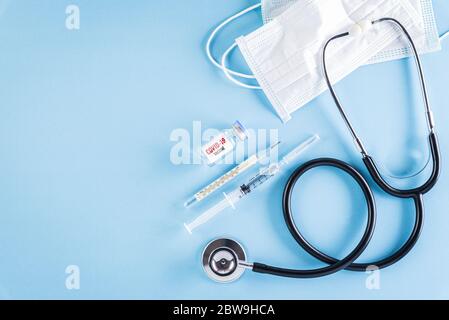 Concetto sanitario e medico. Stetoscopio con maschera protettiva per iniezione o maschera medica e vaccino su sfondo blu. Proteggere Coronav Foto Stock