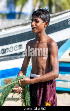 Un giovane pescatore aiuta a distendersi reti da pesca sulla spiaggia di Arugam Bay nello Sri Lanka nella mattina presto. Foto Stock