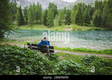 Svizzera, Bravuogn, Palpuognasee, giovane donna che riposa sulla panchina vicino al lago Palpuognasee nelle Alpi svizzere Foto Stock