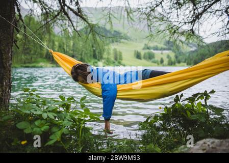 Svizzera, Bravuogn, Palpuognasee, giovane donna che riposa in amaca vicino al lago Palpuognasee nelle Alpi svizzere Foto Stock