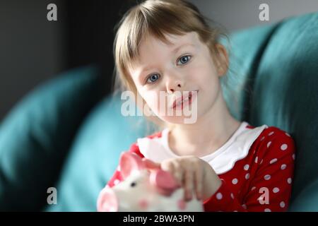 Bambina seduta in divano a casa con banca piggy Foto Stock