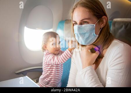 coronavirus covid-19 asia concetto di sicurezza di volo. una giovane madre in una sedia di aeroplano in una maschera respiratoria medica, un bambino carino si siede accanto a lei e. Foto Stock