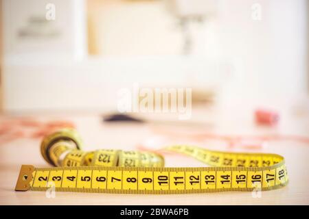 Misuratore di colore giallo su scrivania Seamstress con diversi accessori sullo sfondo della macchina da cucire in sfocatura Foto Stock