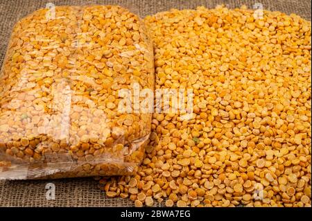 Piselli spezzati gialli in un sacchetto di plastica e cereali sfusi su uno sfondo di tela con una consistenza ruvida. Cereali tradizionali per la preparazione di zuppe e porridg Foto Stock