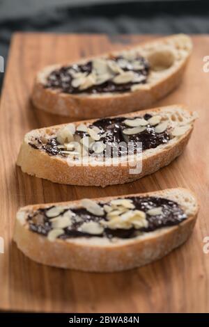 prima colazione dolce ciabatta con crema di nocciole al cioccolato e fiocchi di mandorle su tavola di legno Foto Stock