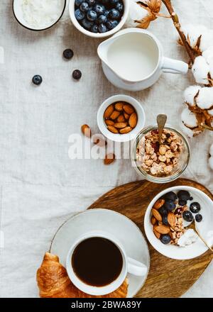 Tavolo per la colazione con muesli, mandorle, mirtillo, fiocchi di cocco, latte, caffè e croissant. Foto Stock