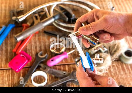 Idraulico mettendo un nastro di teflon, closeup. Attrezzi idraulici sul tavolo da officina. Riparazione dei tubi dell'acqua. Filettatura di tenuta Foto Stock
