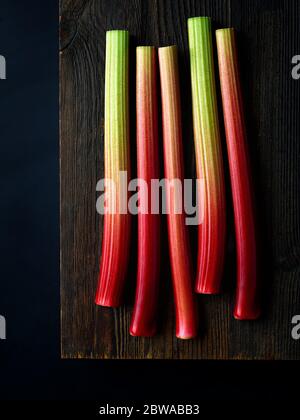 Gambi di rabarbaro freschi su tavola di legno pronti per tritare, sfondo nero, vista dall'alto Foto Stock