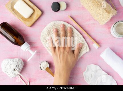 Accessori per bagno zero rifiuti sapone, spazzolino da denti, dentifricio, burro di karité, panno per lavaggi in loofah, contenitore in vetro riutilizzabile. Mano femminile sulla parte superiore. Vista dall'alto, layout. Foto Stock