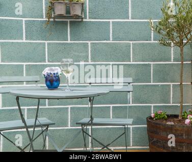 Tavolo e sedie da patio con bicchiere di vino e caraffa in ceramica. Aprile 2020 Foto Stock