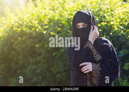 Donna islamica in abiti orientali si trova sullo sfondo di fitti cespugli verdi Foto Stock