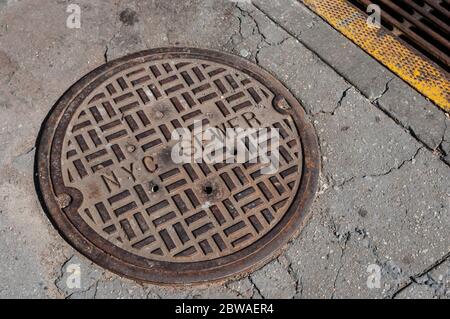 La copertura di tombino in metallo segnava la fogna di New York in un marciapiede a Brooklyn, New York City, New York, USA. Infrastruttura. Coperchio fognario. Foto Stock