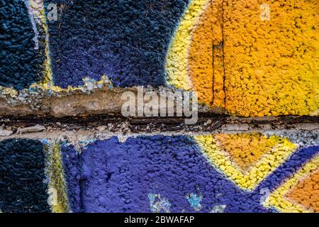 Graffiti primo piano su una struttura di parete in blocchi di cemento fessurato. Street art background. Viola, giallo, nero. Foto Stock
