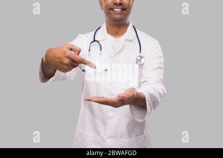 Medico che punta a mano aperta vuota davanti a torace Close Up isolato. Concetto di pubblicità del medico dell'uomo indiano Foto Stock