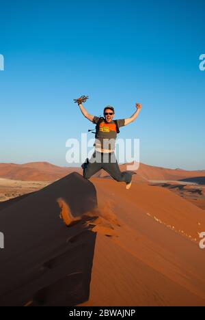 Giovane felice che salta sulla cima di una duna di sabbia del deserto vicino a Sossusvlei in Namibia, Africa. Foto Stock