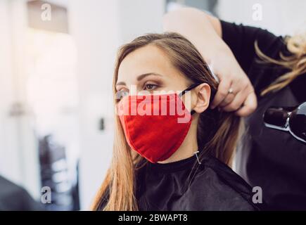 Donna che indossa una maschera rossa per il viso che si sta facendo styling fresco in un parrucchiere Foto Stock