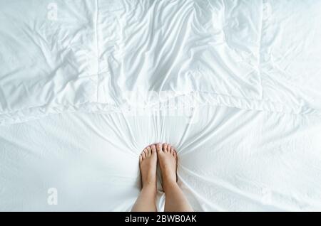 Piedi e piedi simmetricamente passo sui fogli bianchi rugosi del letto. Foto Stock