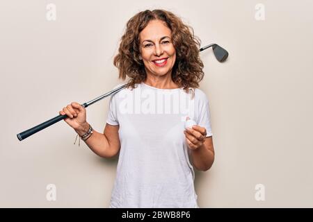 Media età bella sportivo che gioca a golf usando bastone e palla su sfondo bianco guardando positivo e felice in piedi e sorridendo con un confido Foto Stock