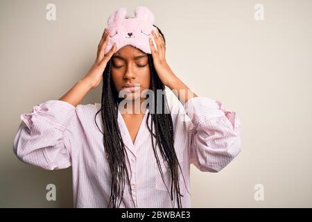 Giovane donna afroamericana che indossa pajama rosa e maschera di sonno su sfondo isolato con la mano sulla testa per il dolore alla testa perché lo stress. Sofferenza Foto Stock