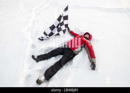 L'uomo giace nella neve con la bandiera del traguardo Foto Stock